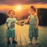 Duas crianças de mãos dadas ao pôr do sol, simbolizando união e crescimento juntos.