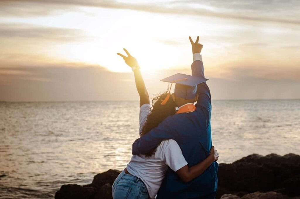 Duas pessoas celebram um momento de realização pessoal ao pôr do sol na praia, simbolizando a descoberta e o crescimento individual no caminho para concretizar objetivos pessoais.