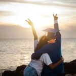 Duas pessoas celebram um momento de realização pessoal ao pôr do sol na praia, simbolizando a descoberta e o crescimento individual no caminho para concretizar objetivos pessoais.