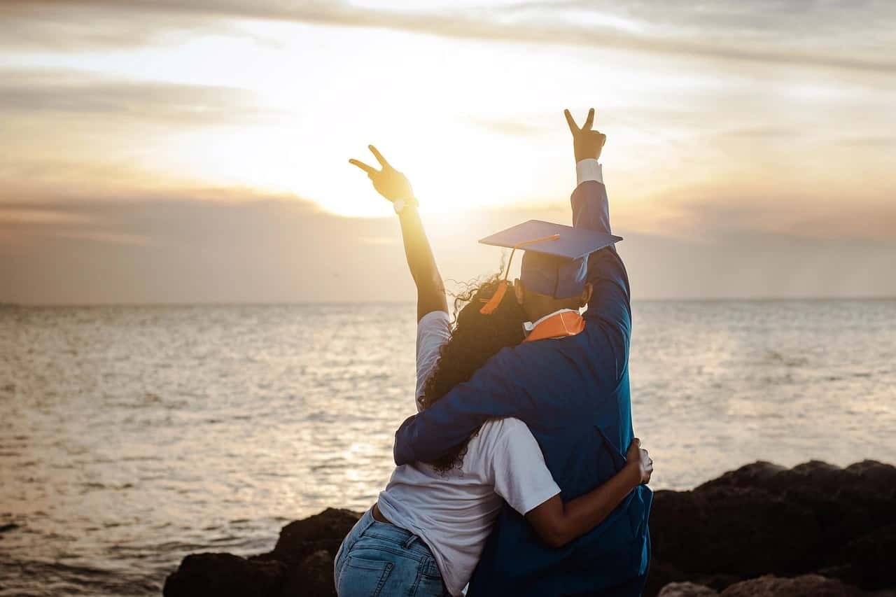 Duas pessoas celebram um momento de realização pessoal ao pôr do sol na praia, simbolizando a descoberta e o crescimento individual no caminho para concretizar objetivos pessoais.