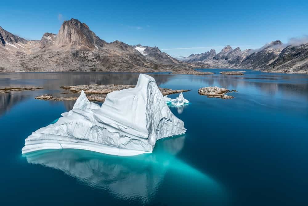 Ilustração de um iceberg representando a persistência e a busca pelo desenvolvimento do potencial escondido. Imagem de um iceberg em águas azuis límpidas com montanhas ao fundo” é ideal para ilustrar o artigo sobre realização de sonhos e desenvolvimento pessoal. Essa imagem simboliza a capacidade oculta de superação e crescimento pessoal no contexto do autoconhecimento.