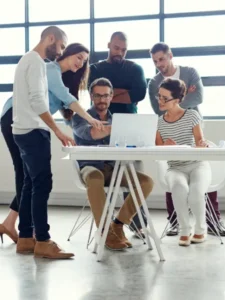 Imagem de um grupo de pessoas conversando; duas delas fornecem feedbacks para as outras que olham para a tela do notebook.