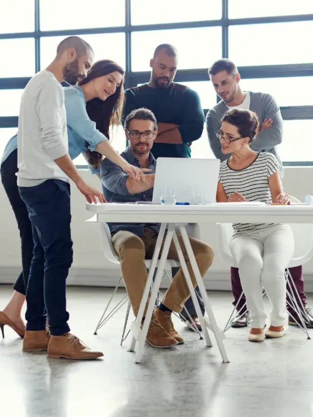 Imagem de um grupo de pessoas conversando; duas delas fornecem feedbacks para as outras que olham para a tela do notebook.