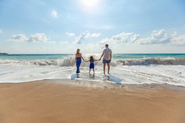 Família de mãos dadas contemplando o mar tranquilo, representando a paz interior e o equilíbrio encontrados no desenvolvimento pessoal.