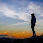 Caminhando em direção ao horizonte luminoso, encontramos a plenitude na jornada da fé. Cada passo é uma descoberta, cada obstáculo uma oportunidade de crescimento. Que a luz que guia nosso caminho nos inspire a perseguir a verdade, a esperança e a realização de nossos mais profundos anseios. Silhueta de pessoa contemplando pôr do sol inspirador” para o artigo sobre decisões sábias e plenitude em “Desvende a Fé”, categoria “Alcance a Plenitude”, subcategoria “Desenvolvimento Individual.