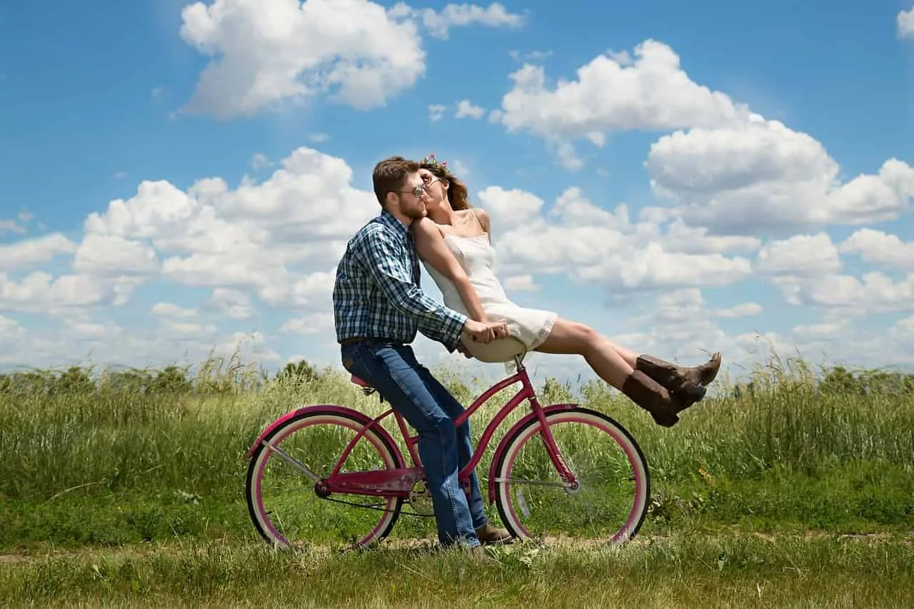 Casal compartilhando um momento de intimidade e felicidade em uma bicicleta no campo sob um céu azul - desenvolvimento pessoal e emocional.