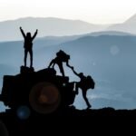 Três alpinistas conquistam o pico da montanha ao amanhecer, simbolizando sucesso e positividade no artigo ‘Poder Mental Supera o Físico’ - destacando atitudes vencedoras para alcançar o sucesso.