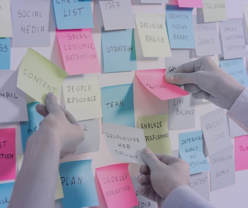 Quadro com post-its coloridos contendo palavras-chave como estratégia, decisão e análise de desempenho, com duas mãos interagindo. Imagem do artigo "Supere Seus Obstáculos: O Início", da categoria "Supere Seus Obstáculos". Ideal para conteúdos sobre organização, planejamento estratégico e gestão eficiente de tarefas.