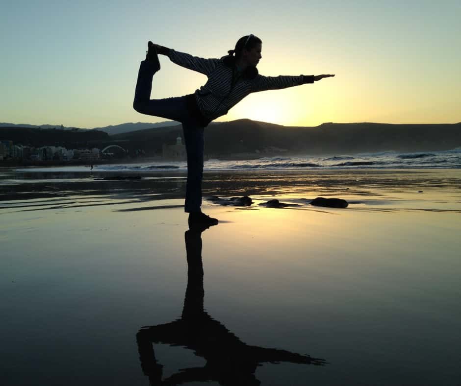 Pessoa praticando yoga na praia ao pôr do sol, executando a pose "Natarajasana" ou "Pose do Dançarino", representando equilíbrio emocional e superação de frustrações. Imagem do artigo "Expectativas: Frustrações em Potencial", categoria "Desenvolvimento Pessoal" e subcategoria "Desenvolvimento Emocional".